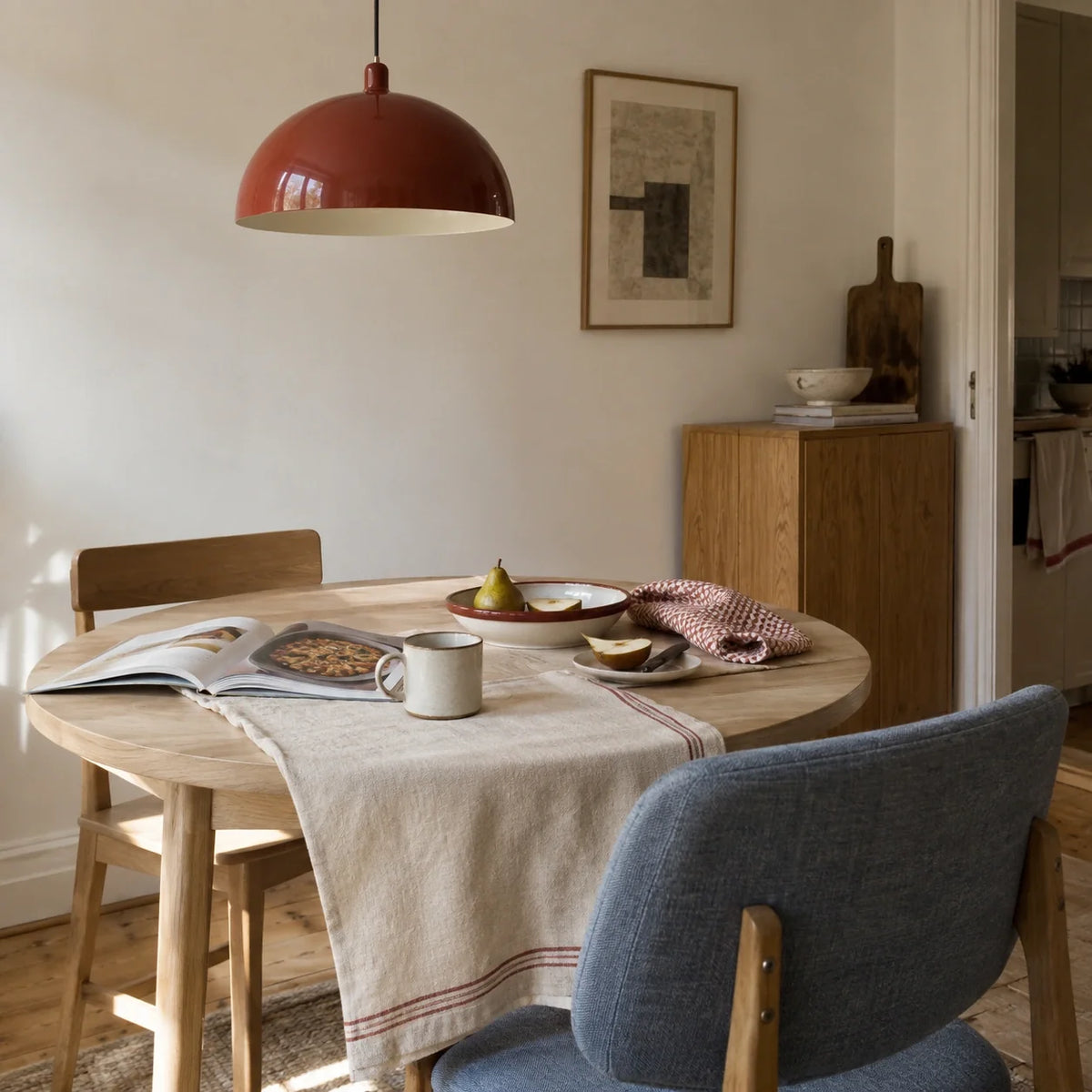 Brick-red dome pendant with pale wood and blue-grey seating in a dining nook