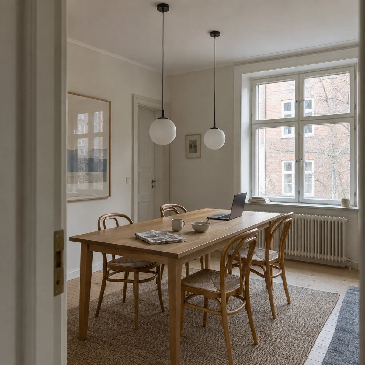 Two small globe pendants above a long dining table in a daylight apartment