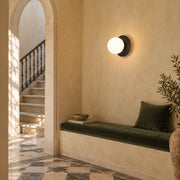 Black disc and single opal-globe wall light above an olive bench in an ochre stair landing