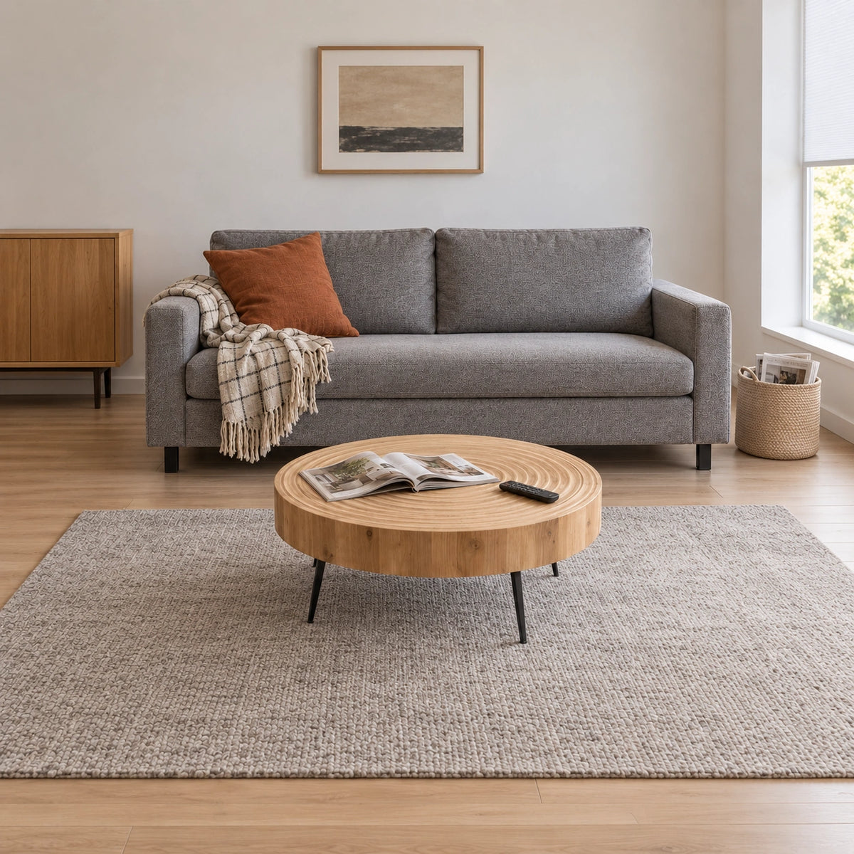 Large fluted round coffee table with magazine and remote beside a full grey sofa