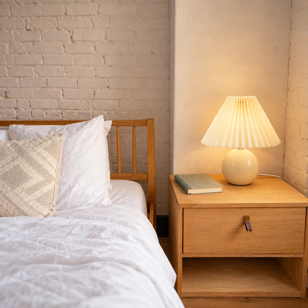 A pleated table lamp adds texture to a calm cream and oak bedroom.