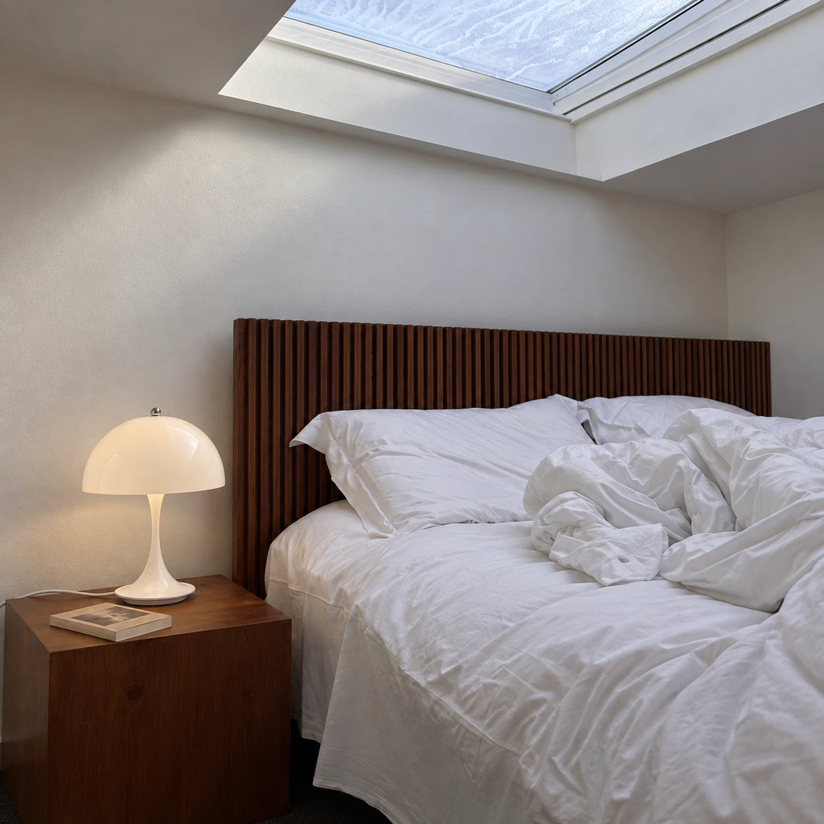 White Dome corded table lamp on a bedside cabinet beside a rumpled bed and skylight