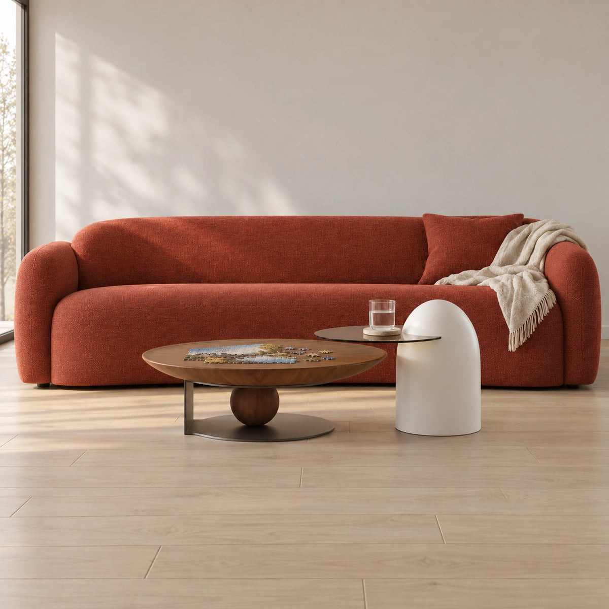 Sculptural two-piece coffee table set with puzzle and water glass in front of a complete rust-coloured sofa